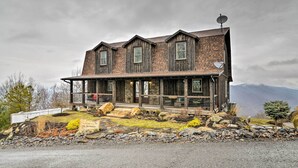 A rustic two-story house with a wooden exterior, a covered porch, and a satellite dish.