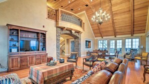 A spacious living room with a high ceiling, a stone fireplace, leather sofas, and a large TV.