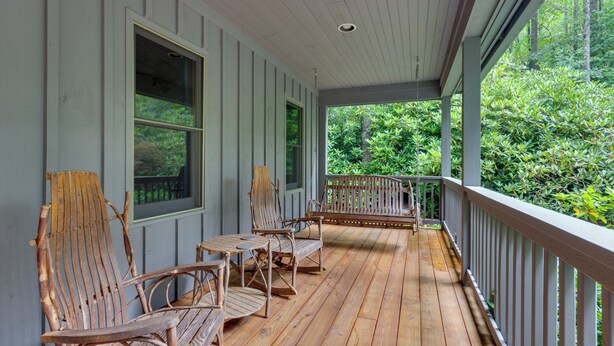 A wooden porch with a railing, two chairs, and a table.