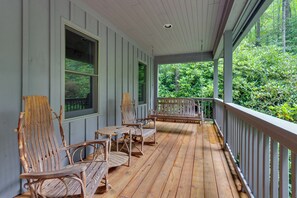 A wooden porch with a railing, two chairs, and a table.
