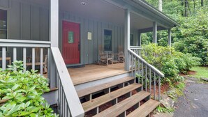 A wooden porch with a red door, a covered seating area with chairs, and a staircase leading up to the entrance.