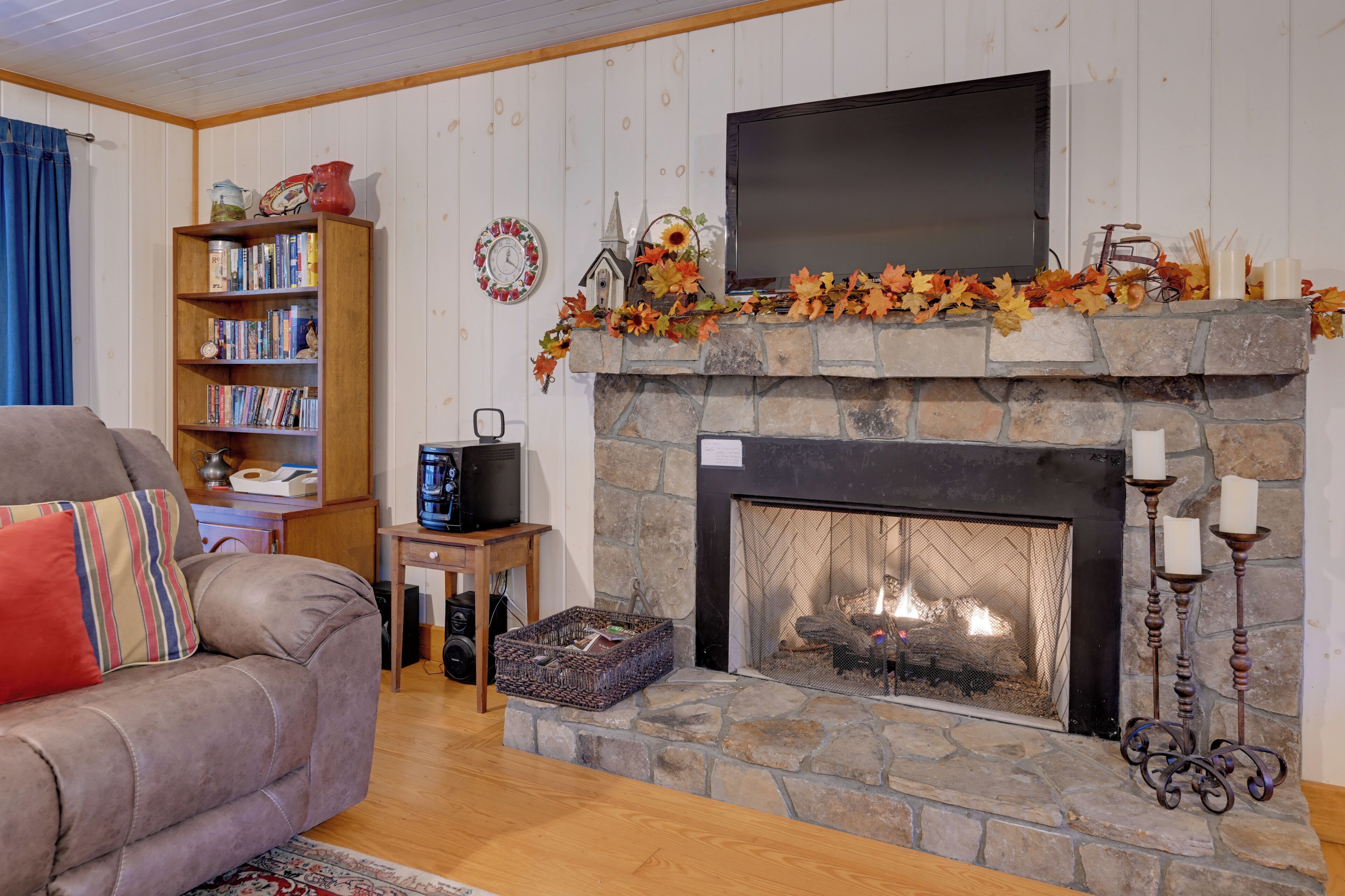 Una sala de estar acogedora con una chimenea de piedra, un televisor montado sobre ella y una estantería llena de libros.