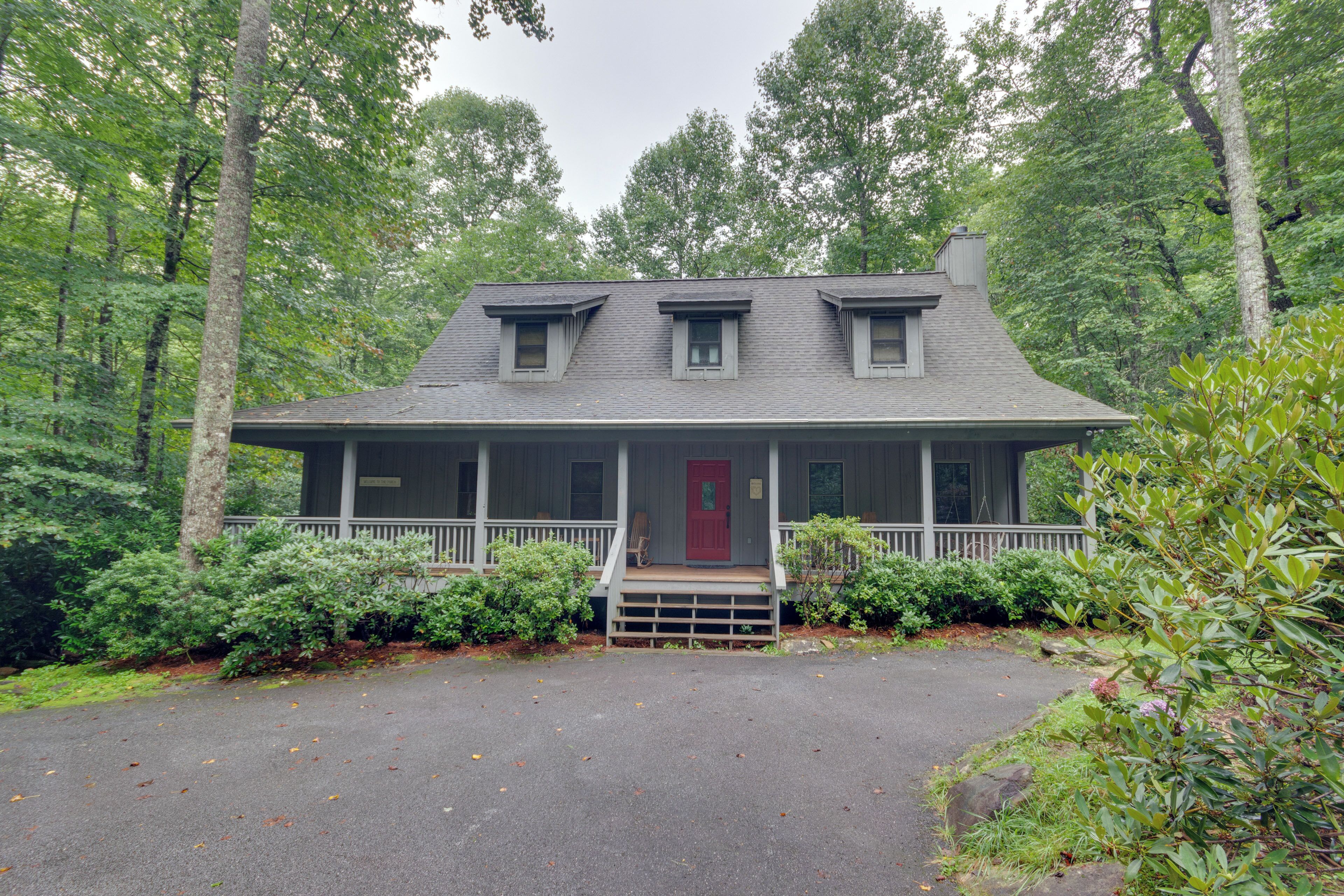 A two-story house with a porch, surrounded by dense forest.