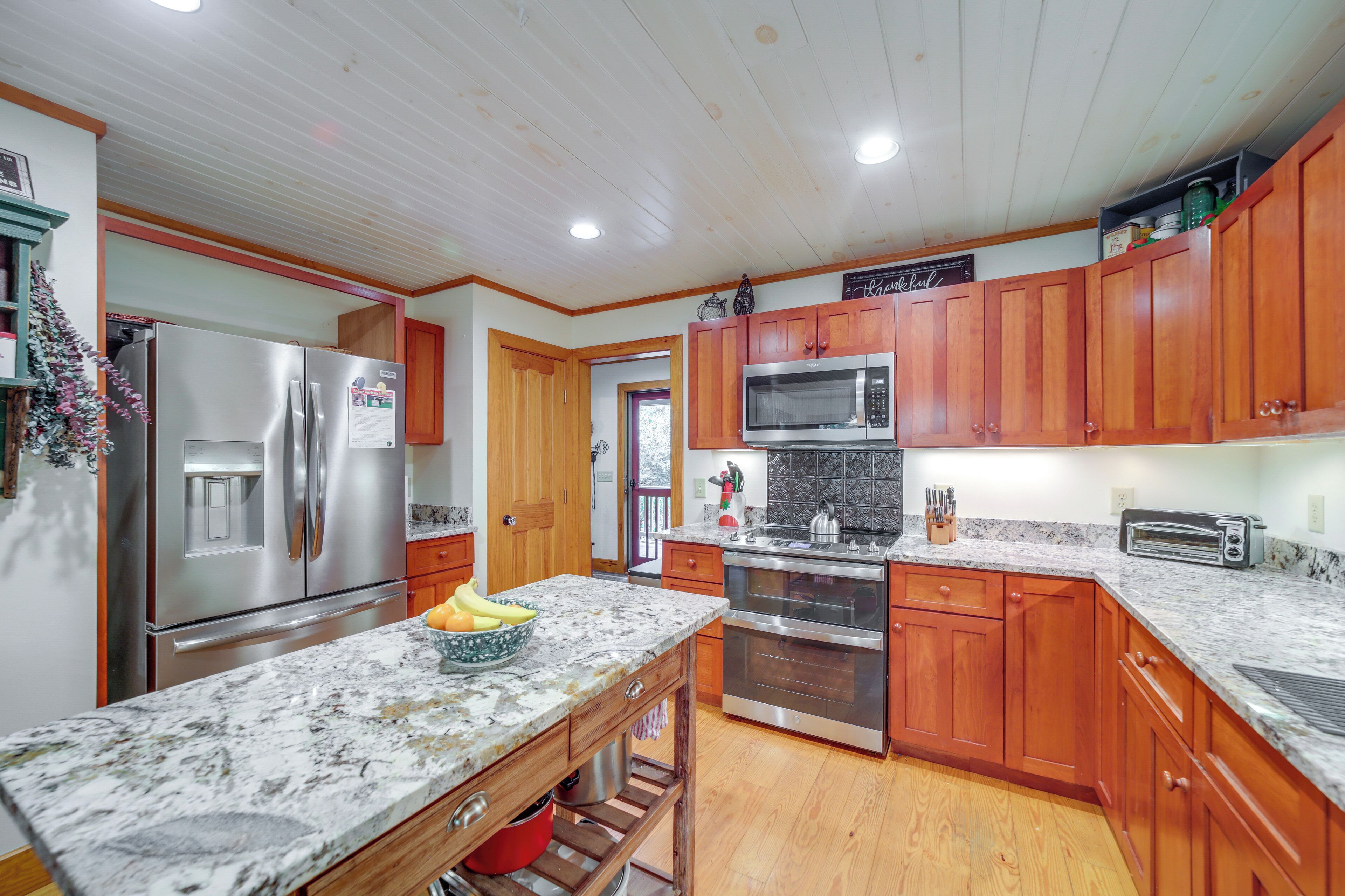 Cocina con armarios de madera, electrodomésticos de acero inoxidable y encimera de mármol.