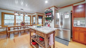 A spacious kitchen with wooden flooring, a marble island, stainless steel appliances, and a large window overlooking a snowy landscape.