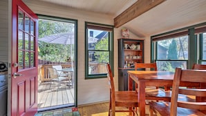 A cozy room with a wooden table and chairs, a red door, and a view of a deck and trees outside. - Walk to Lake George! Bolton Landing Cottage (Bolton Landing)