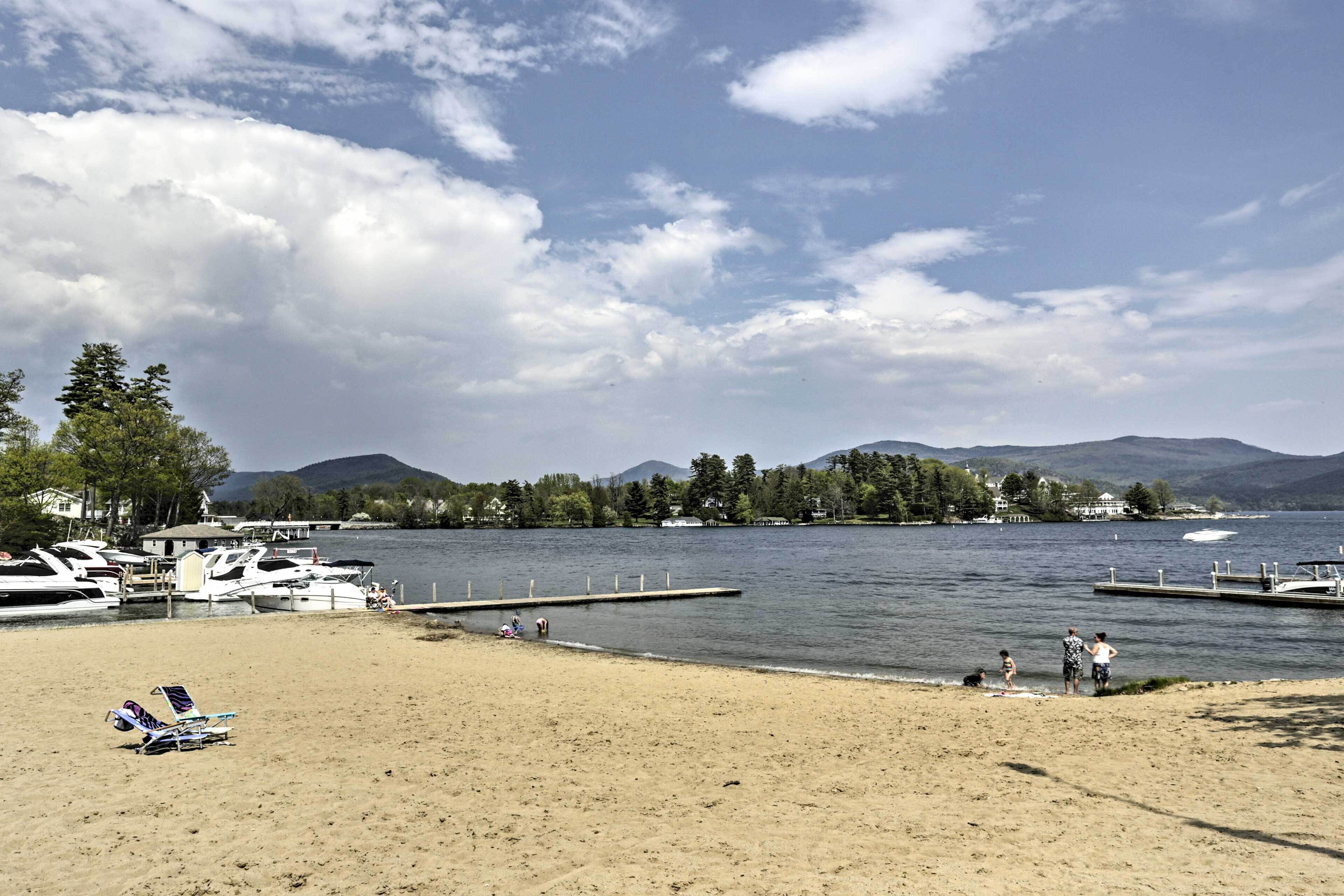 A beach with boats docked, a pier, and mountains in the background.