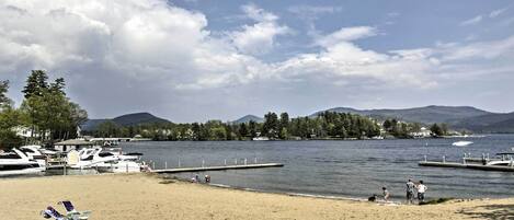 A beach with boats docked, a pier, and mountains in the background.