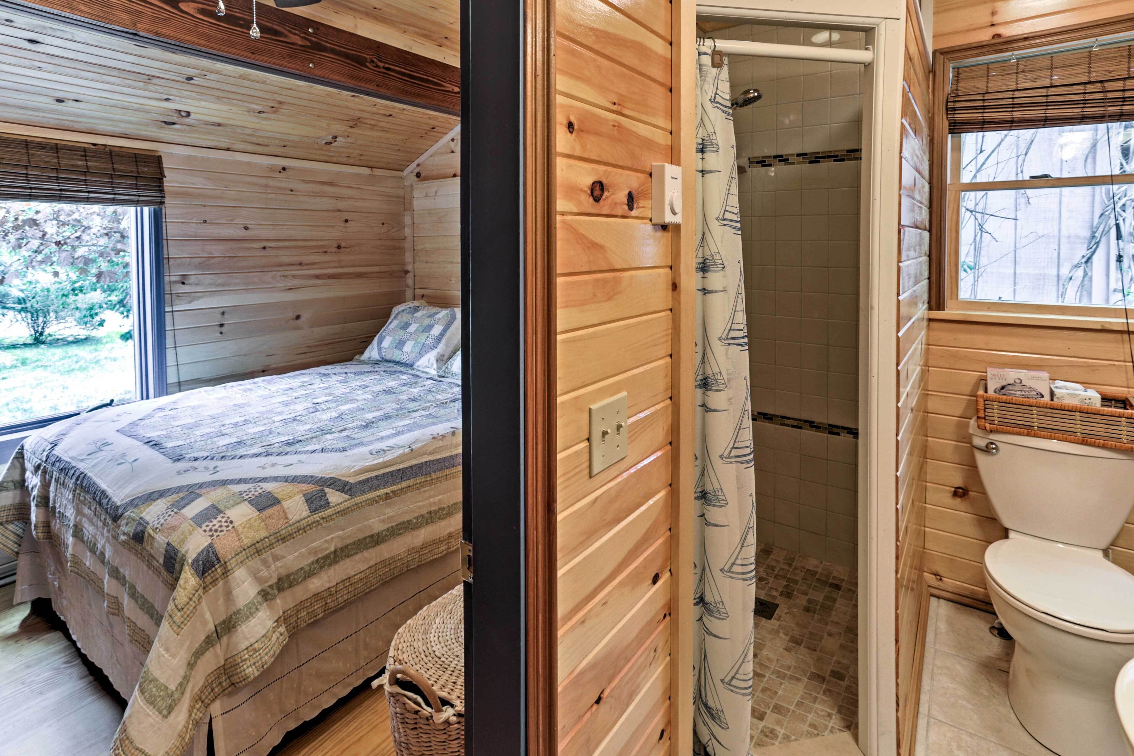 A wooden cabin bedroom with a bed, a window, and a bathroom with a shower and toilet.