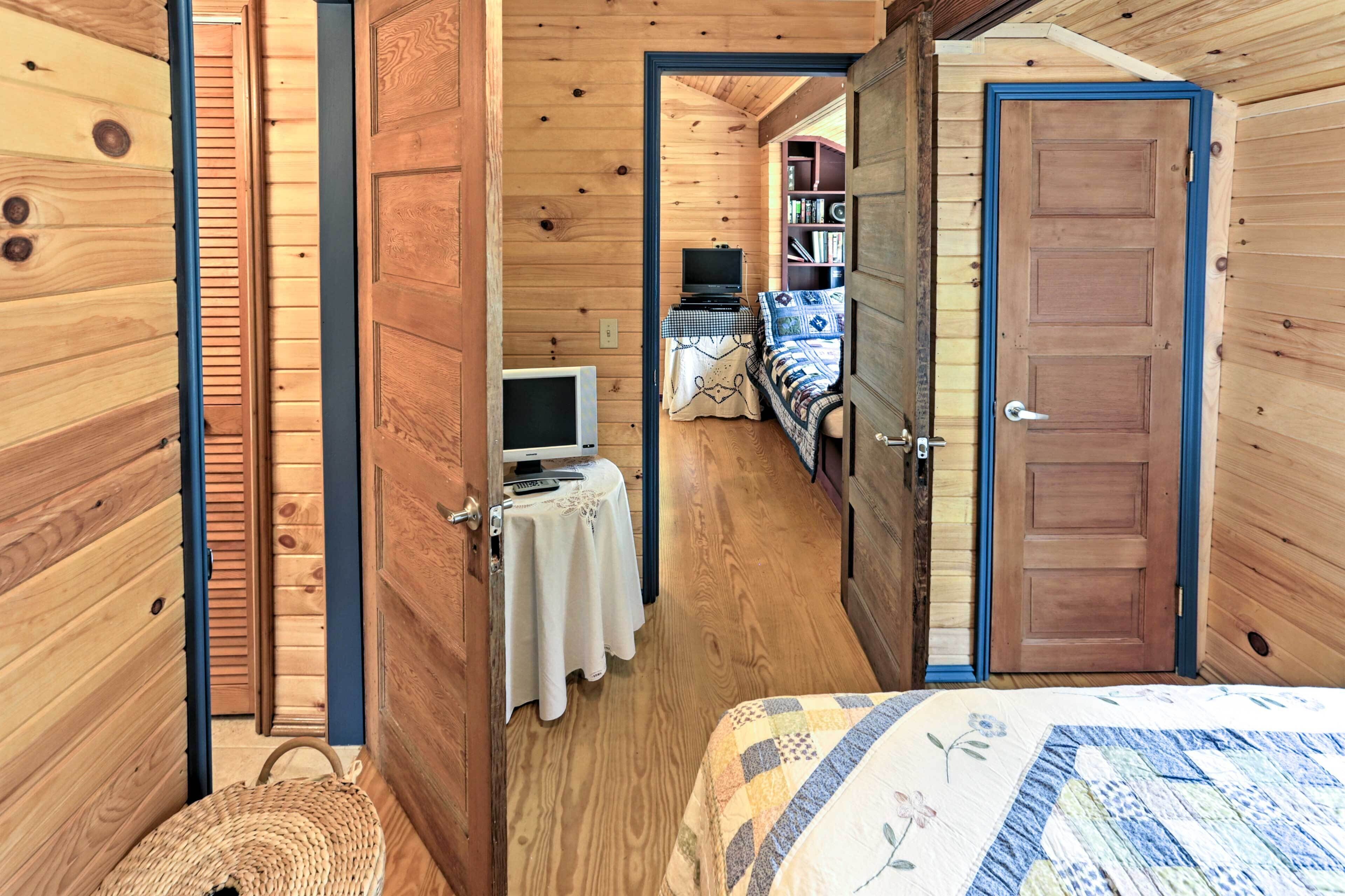 A wooden cabin interior with a bed, a television, and a small table with a lamp.