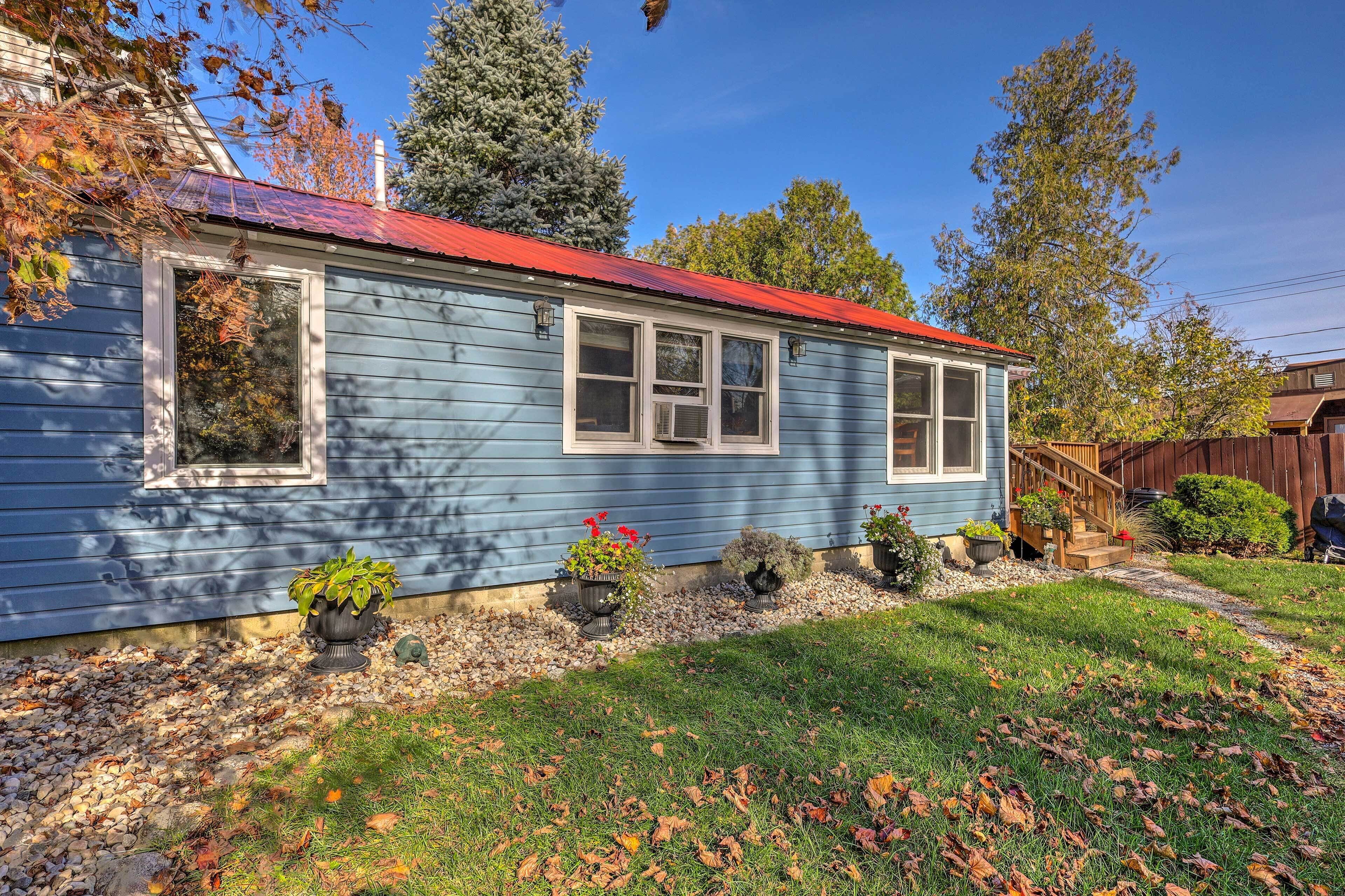 A blue house with a red roof, surrounded by a well-maintained lawn and potted plants.