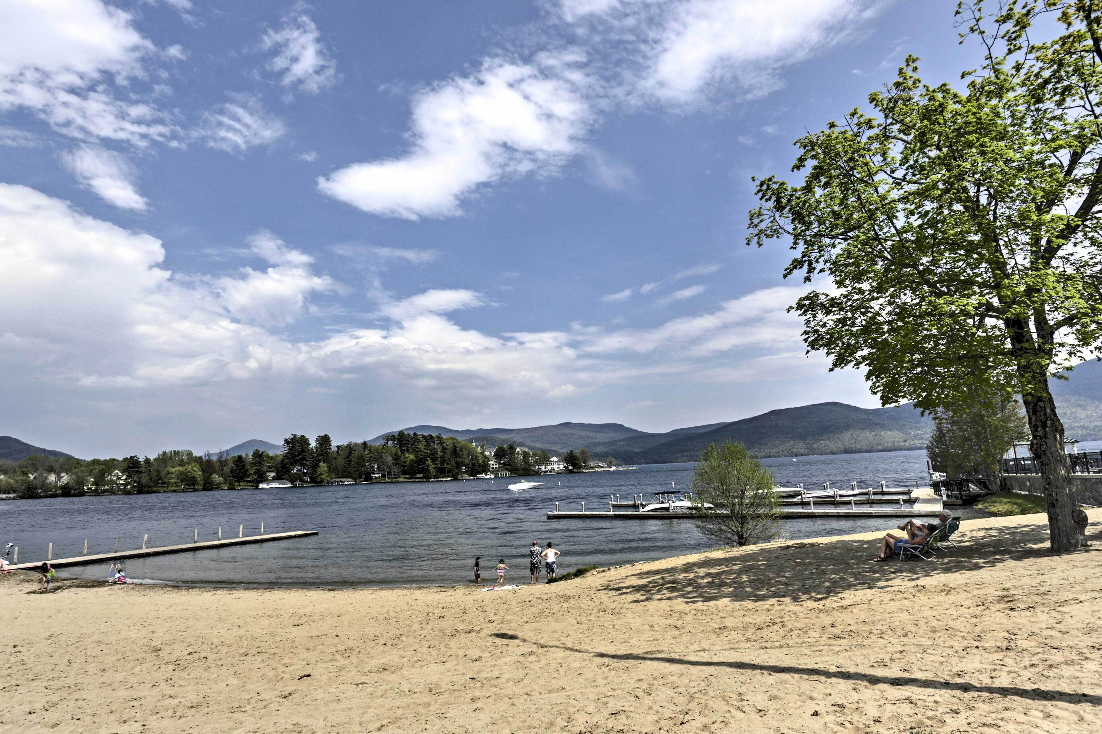 A lakeside beach with a dock, a tree, and a clear sky.