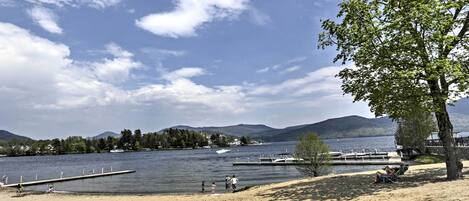 A lakeside beach with a dock, a tree, and a clear sky.