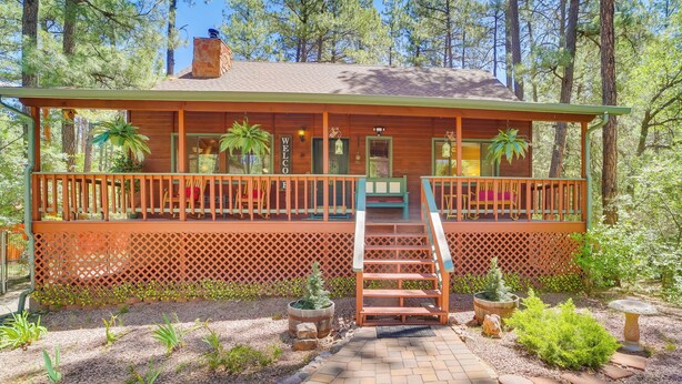 Eine Holzhütte mit Veranda, Treppe und Garten, einschließlich Pflanzen und Vogeltränke.