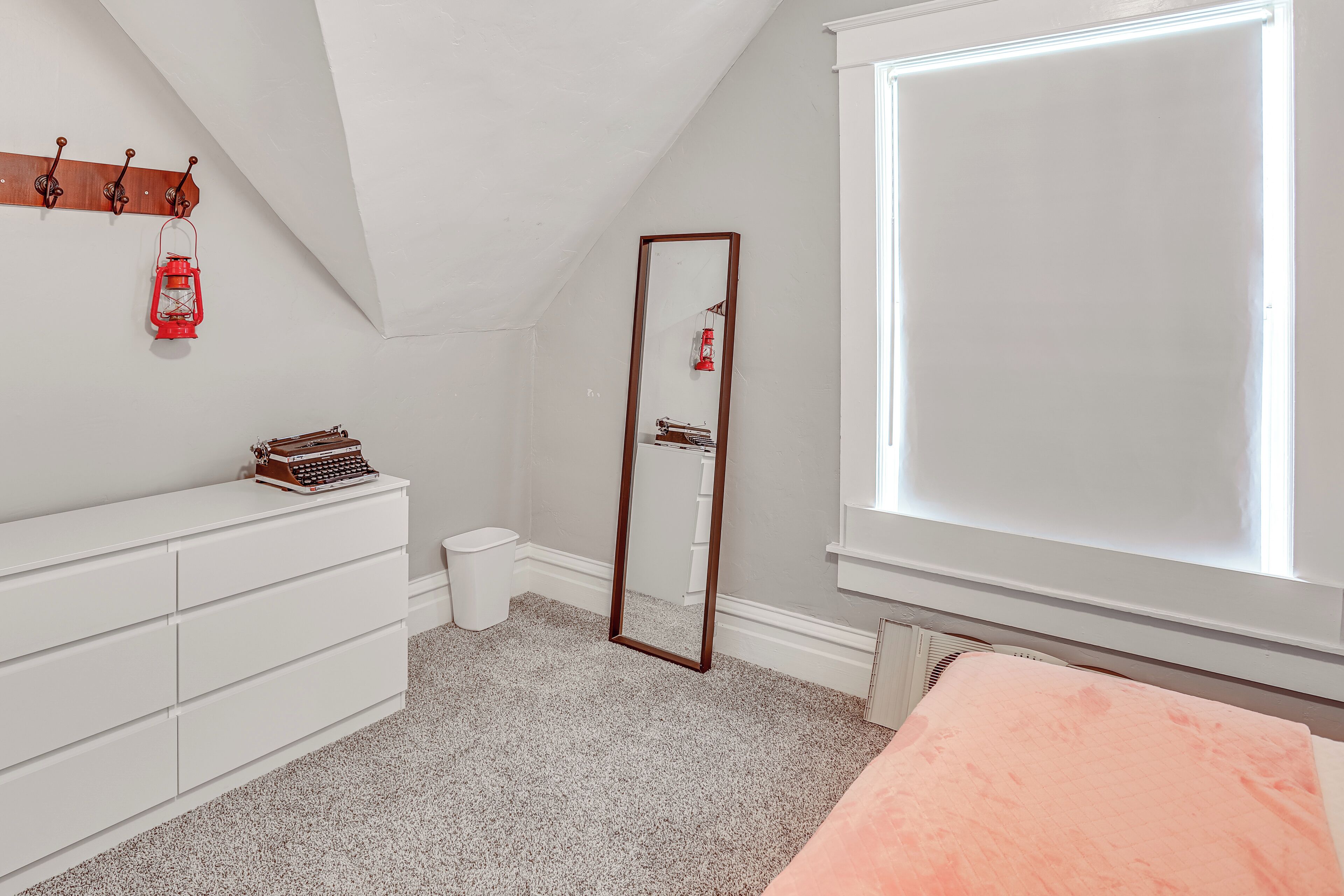 Een slaapkamer met een witte dressoir, een spiegel, een rode lantaarn en een raam met jaloezieën.