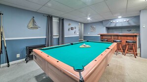 Une table de billard dans une pièce aux murs bleus, avec un coin bar et un plafond doté d’un éclairage encastré.