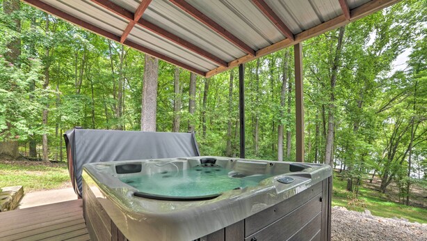 Un bain à remous installé sous une terrasse en bois, surmontée d’un toit en métal, et entouré d’une zone boisée.