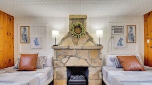 Una habitación con dos camas, una chimenea de piedra y cuadros en las paredes.