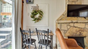 Interior acogedor de una cabaña con chimenea de piedra, un televisor montado encima y una zona de comedor con dos sillas y una mesa.