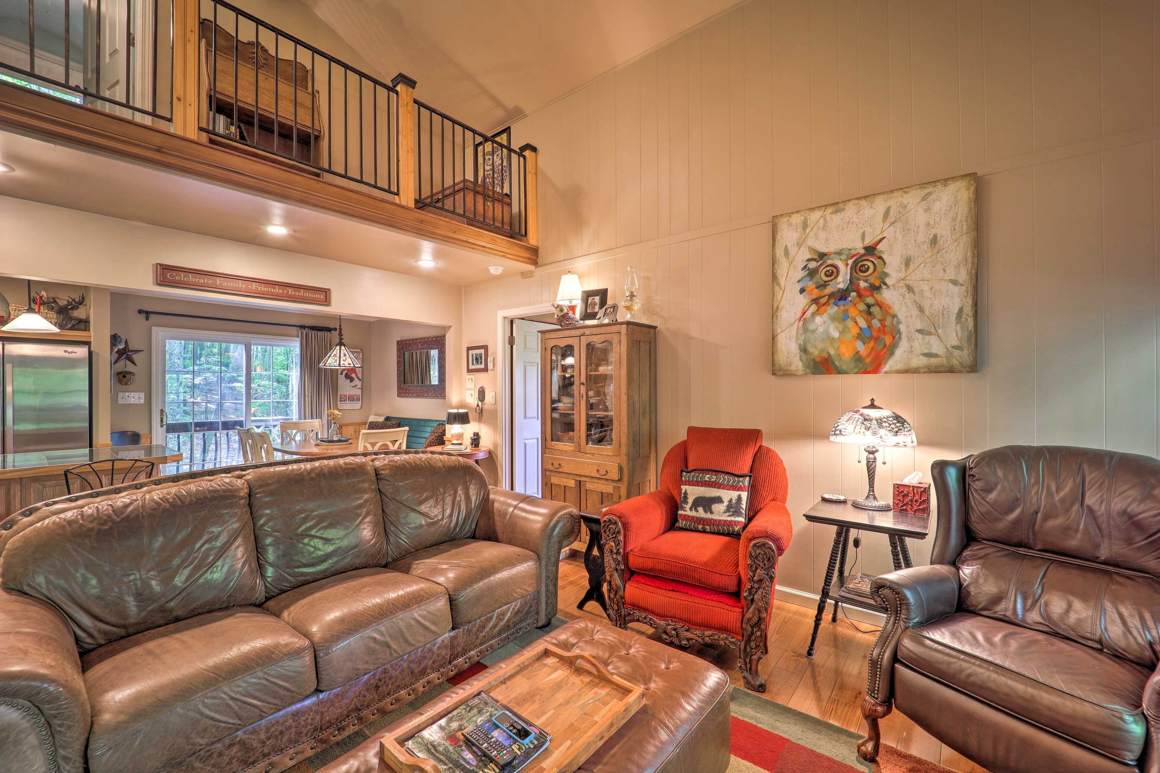 A spacious living room with a high ceiling, leather sofas, a red armchair, and a large painting of an owl.