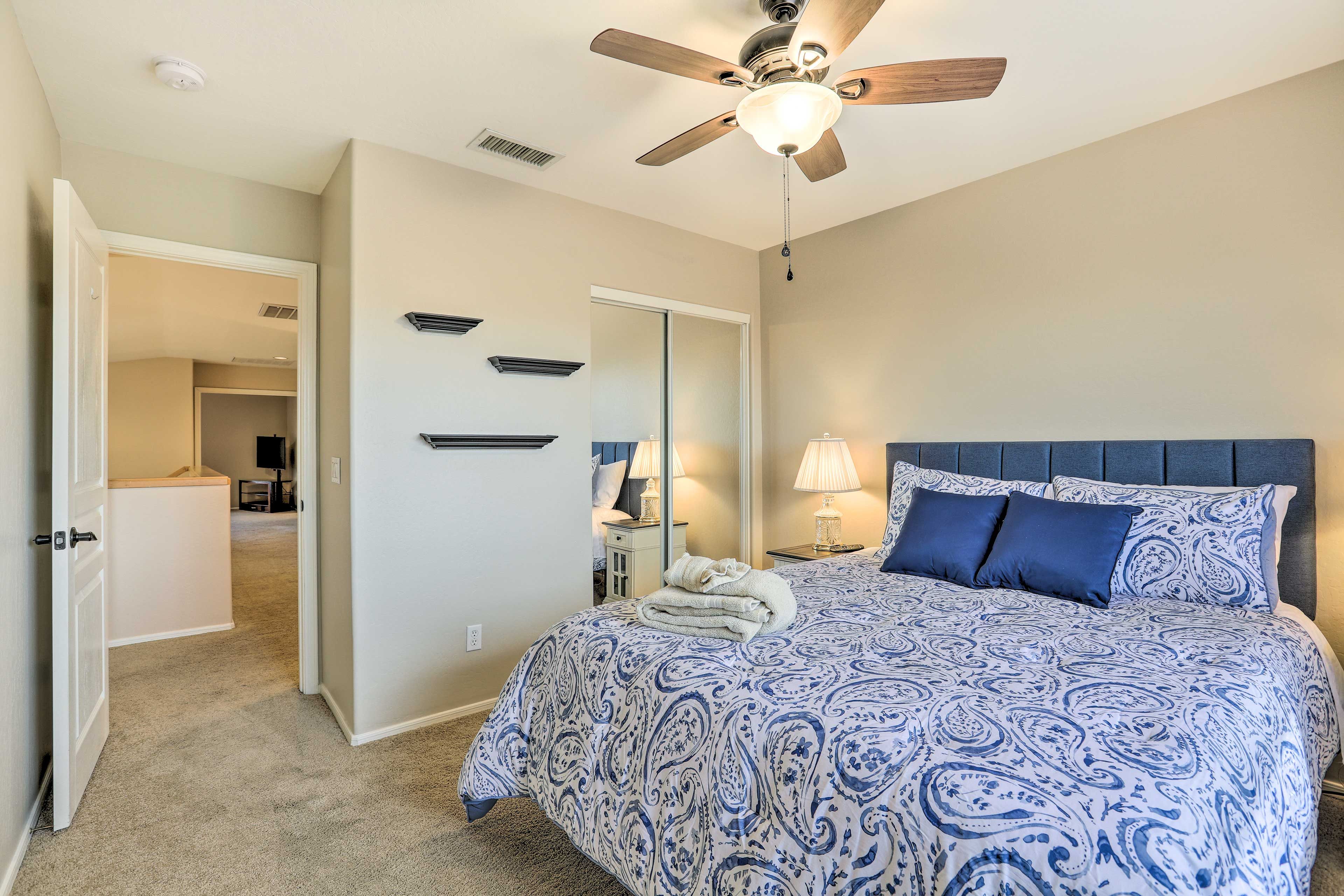 A bedroom with a bed, a ceiling fan, a nightstand, and a mirror.