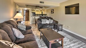 A living room with a sofa, a coffee table, and a TV. There is a kitchen in the background with cabinets and a ceiling fan. - Scottsdale Condo w/ Pool Access: Hike, Swim & Shop (Scottsdale)
