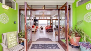 Un interior luminoso con una pared verde, un banco de madera con cojín y vistas a una sala de estar con muebles y una planta grande.
