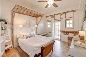 A bedroom with a wooden ceiling, a bed with white bedding, a wicker chair, and a desk with a lamp.