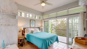 Un dormitorio con cama, mesita de noche, banco de madera, ventana con persianas y ventilador de techo.