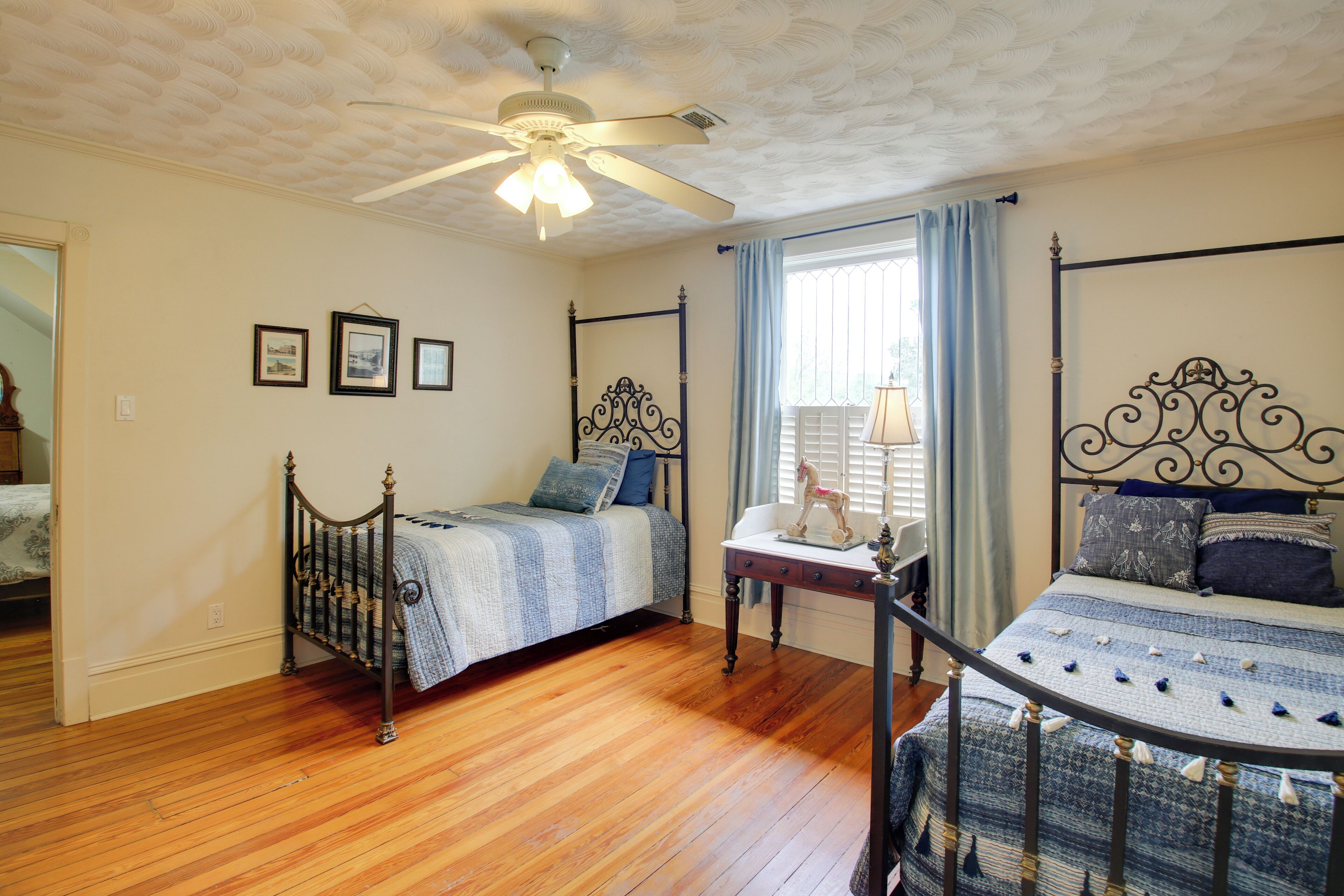 A bedroom with two beds, wooden flooring, a ceiling fan, and framed pictures on the wall.