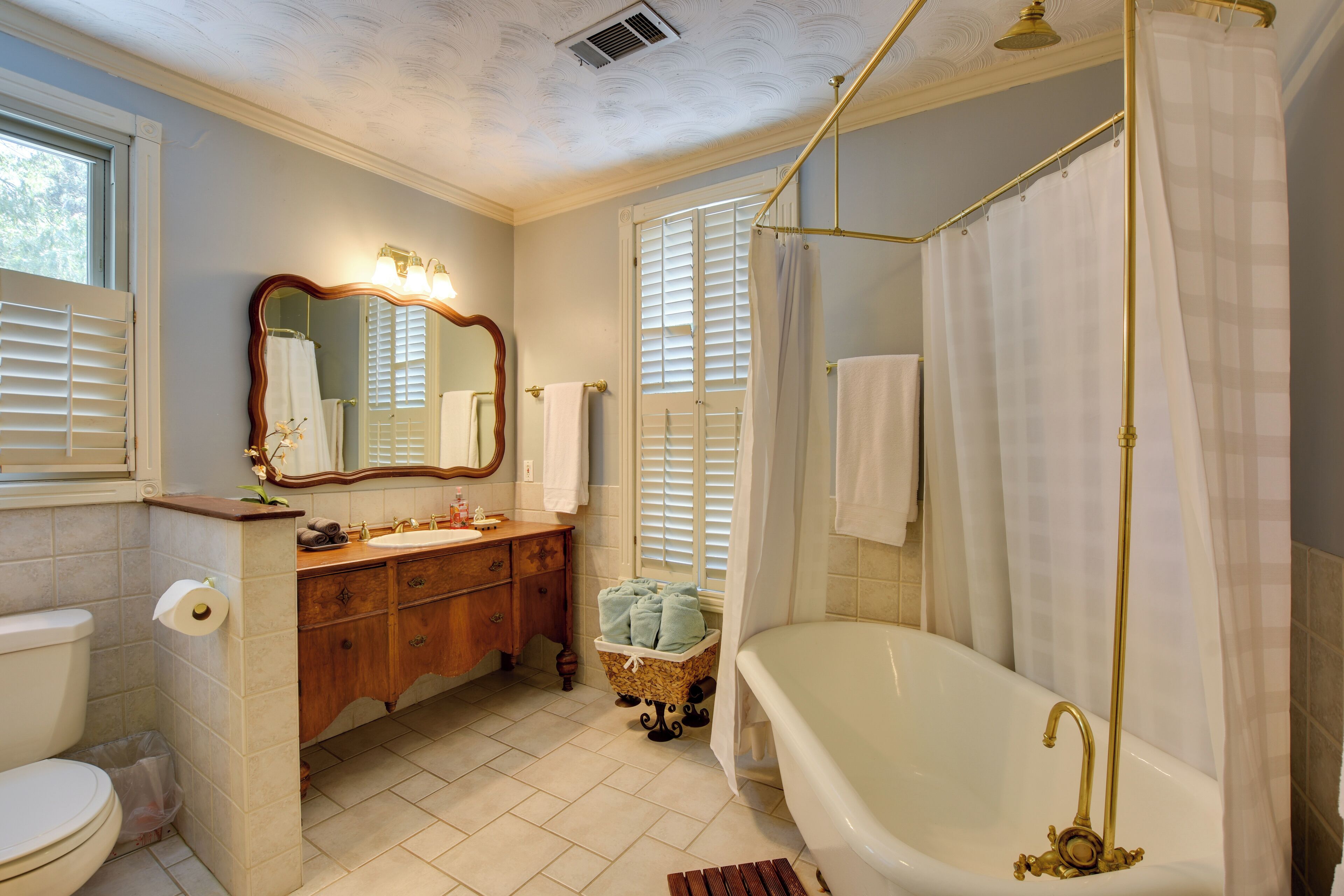 Une salle de bain avec une baignoire, un meuble-lavabo avec un miroir et une fenêtre avec des stores.