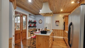 A kitchen with wooden flooring, a central island, wooden cabinets, a refrigerator, and a window with blinds. - Historic Hot Springs Home < 1 Mi to Oaklawn! (Hot Springs)