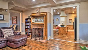 A living room with a fireplace, a leather sofa, and a bookshelf. - Historic Hot Springs Home < 1 Mi to Oaklawn! (Hot Springs)