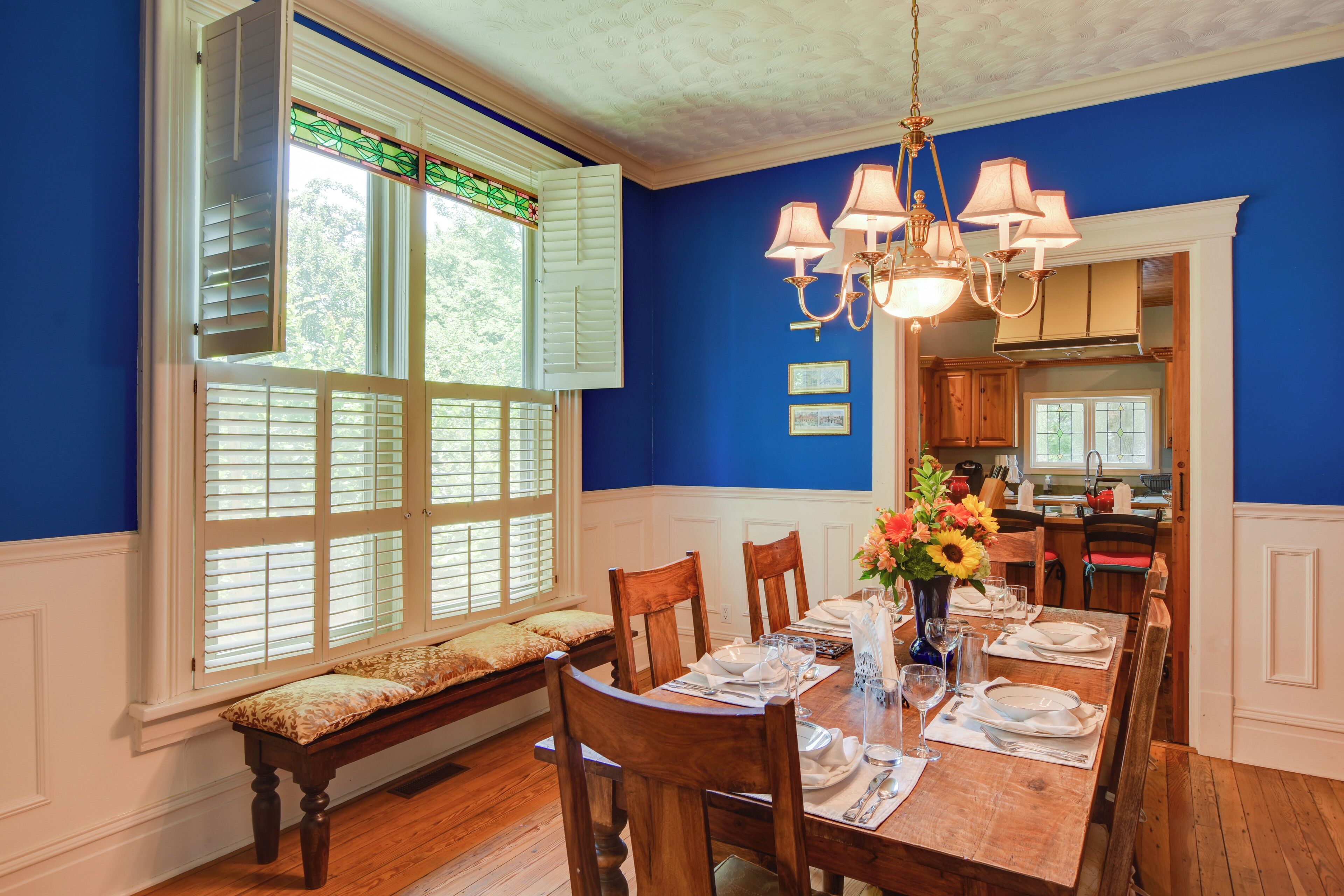 A dining room with a wooden table set for six, a bench, and a window with shutters.
