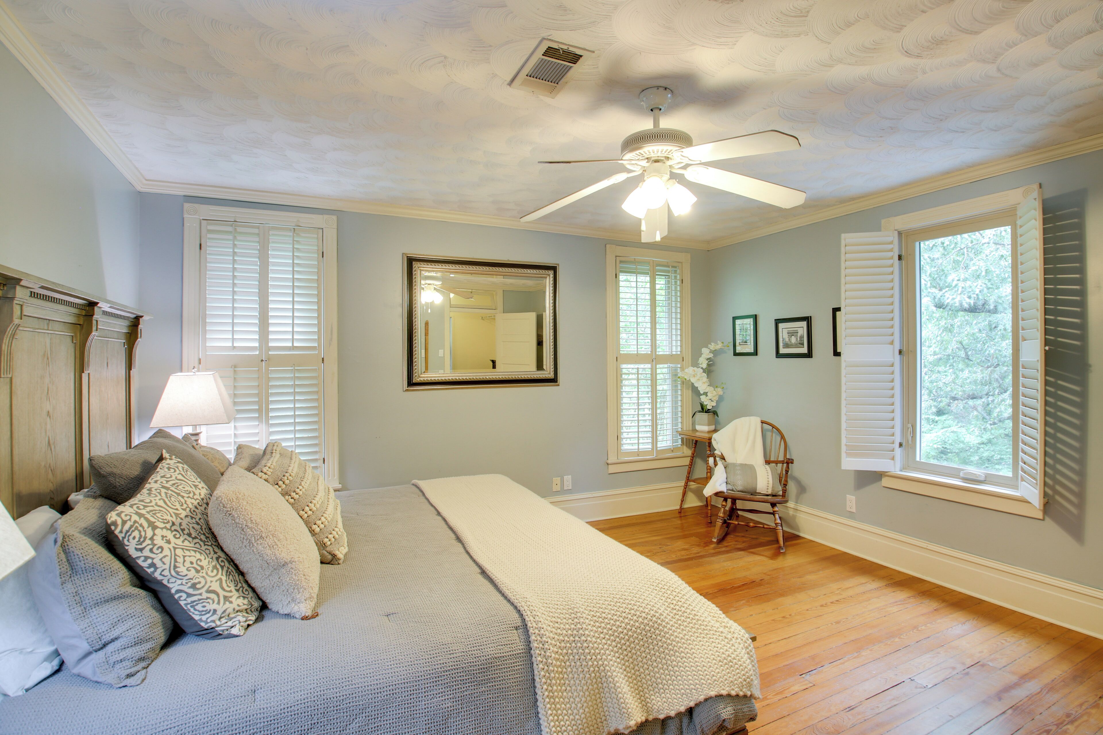 A bedroom with a bed, a ceiling fan, a window with shutters, and a chair.