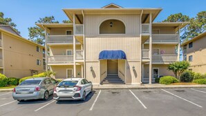 Un immeuble à plusieurs étages doté d’une entrée centrale, de balcons et d’un parking pouvant accueillir deux voitures.