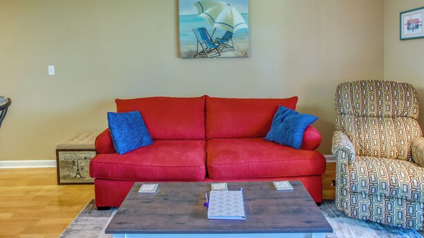 Un salon avec un canapé rouge, un fauteuil à motifs, une table basse et un tableau représentant un voilier.