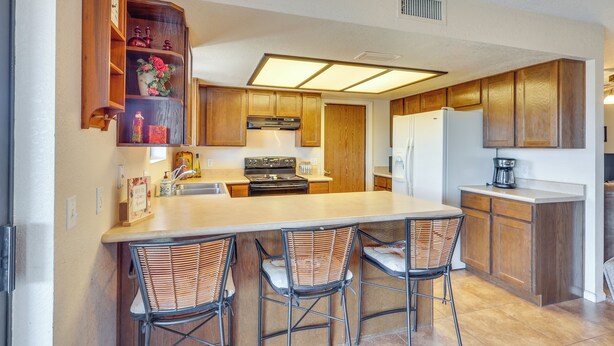 Una cocina con armarios de madera, una isla central con taburetes de bar, un refrigerador y una estufa.