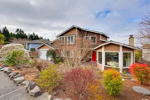 A two-story house with a front porch, a garage, and a well-maintained garden with various shrubs and a small tree. - Washington Vacation Rental w/ Hot Tub Near Tacoma (University Place)