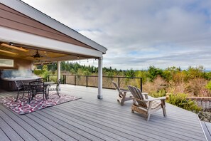 A covered deck with a grill, seating, and a view of the landscape. - Washington Vacation Rental w/ Hot Tub Near Tacoma (University Place)