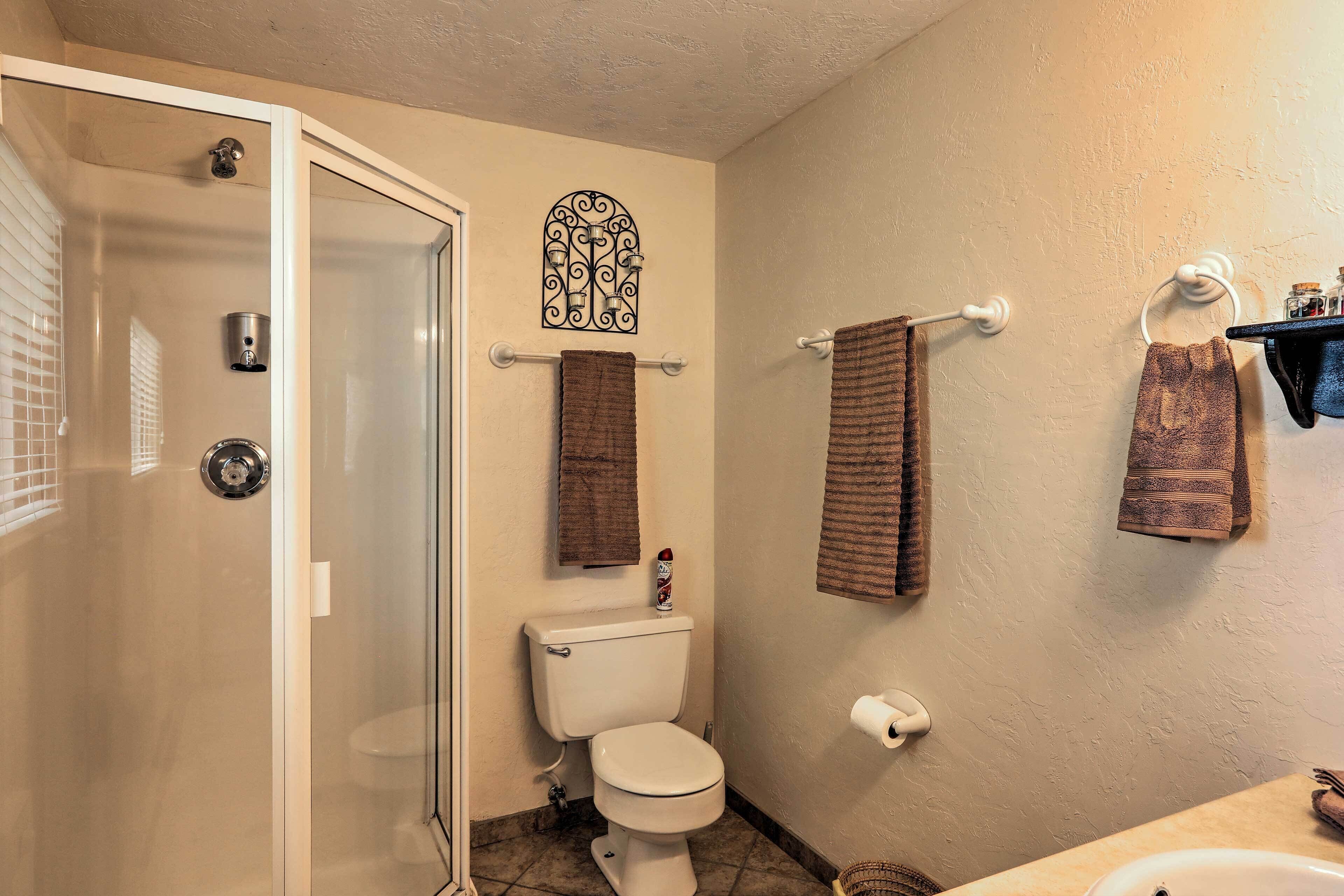 A bathroom with a glass shower door, a toilet, a towel rack, and a shelf with toiletries.
