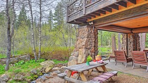 A rustic wooden deck with a stone pillar, picnic table, and outdoor seating area surrounded by a forest.