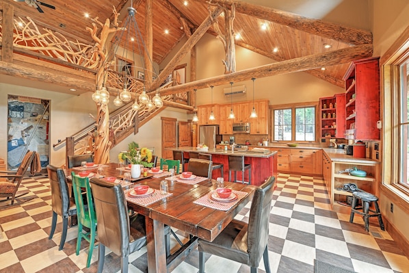 A spacious kitchen with wooden beams, a dining area with a checkered floor, and a staircase with a unique wooden design.
