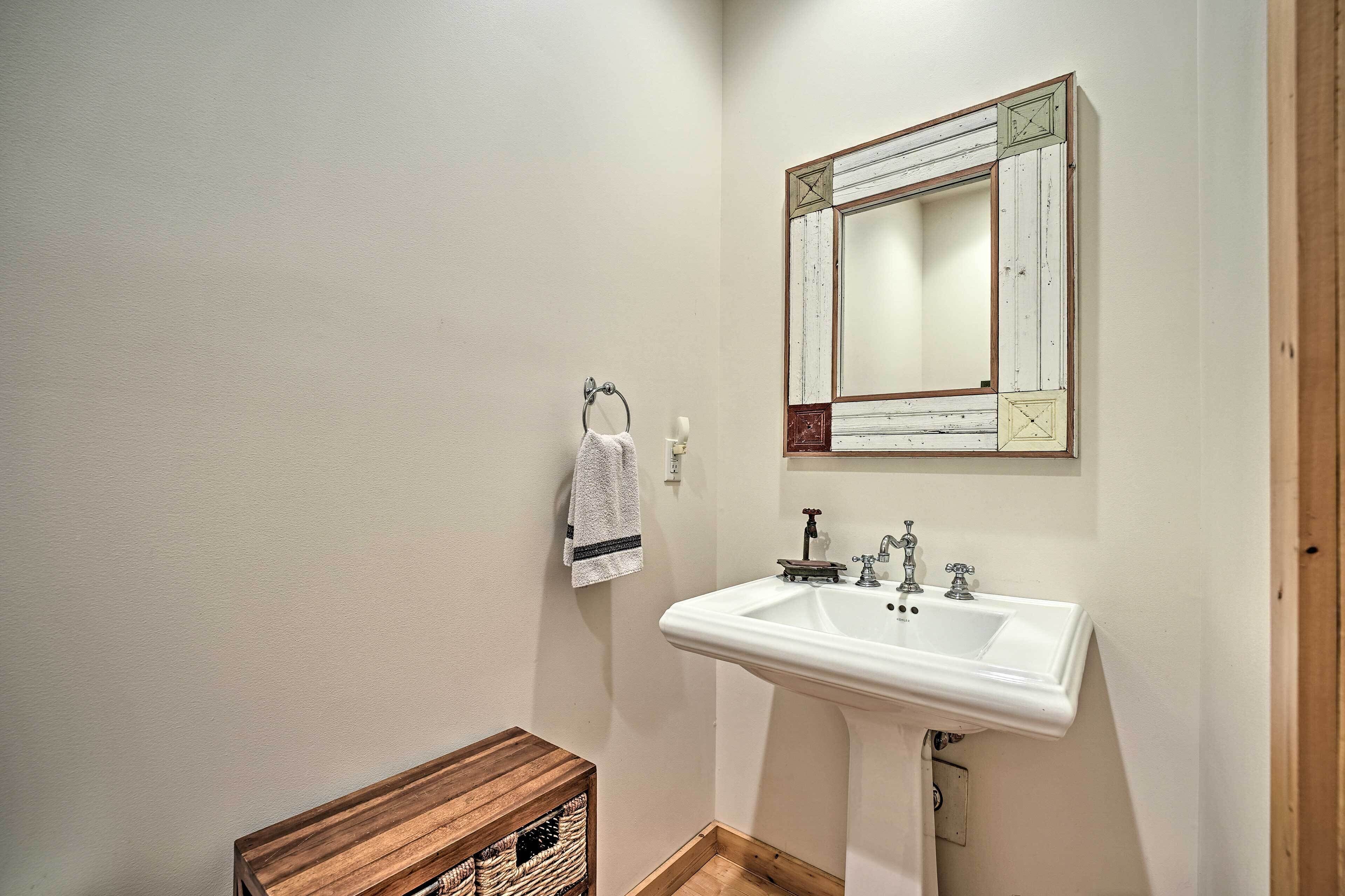 Une salle de bain avec un lavabo blanc, un miroir doté d’un cadre décoratif et une caisse en bois.