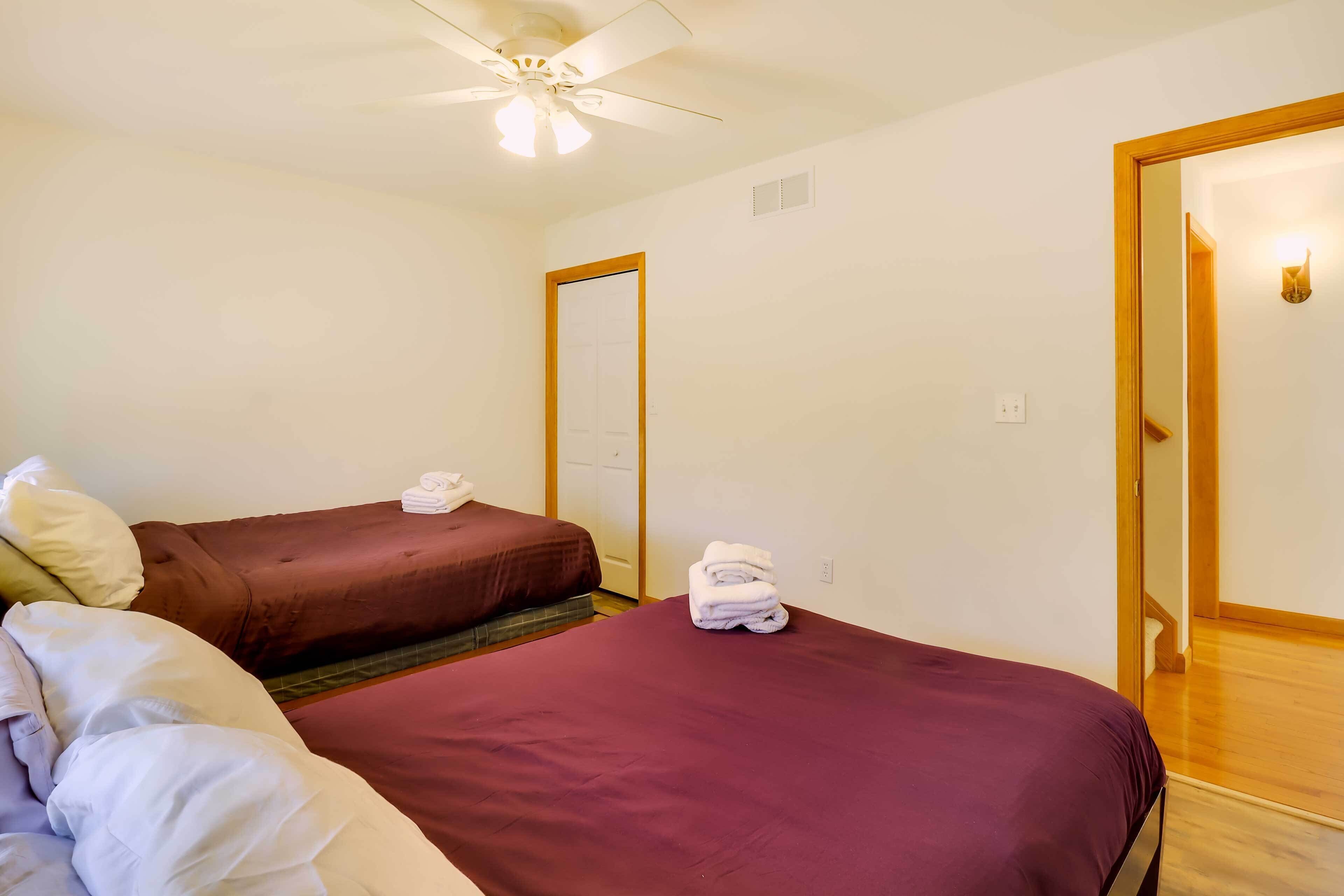 A hotel room with two beds, a ceiling fan, a mirror, and a wooden door.