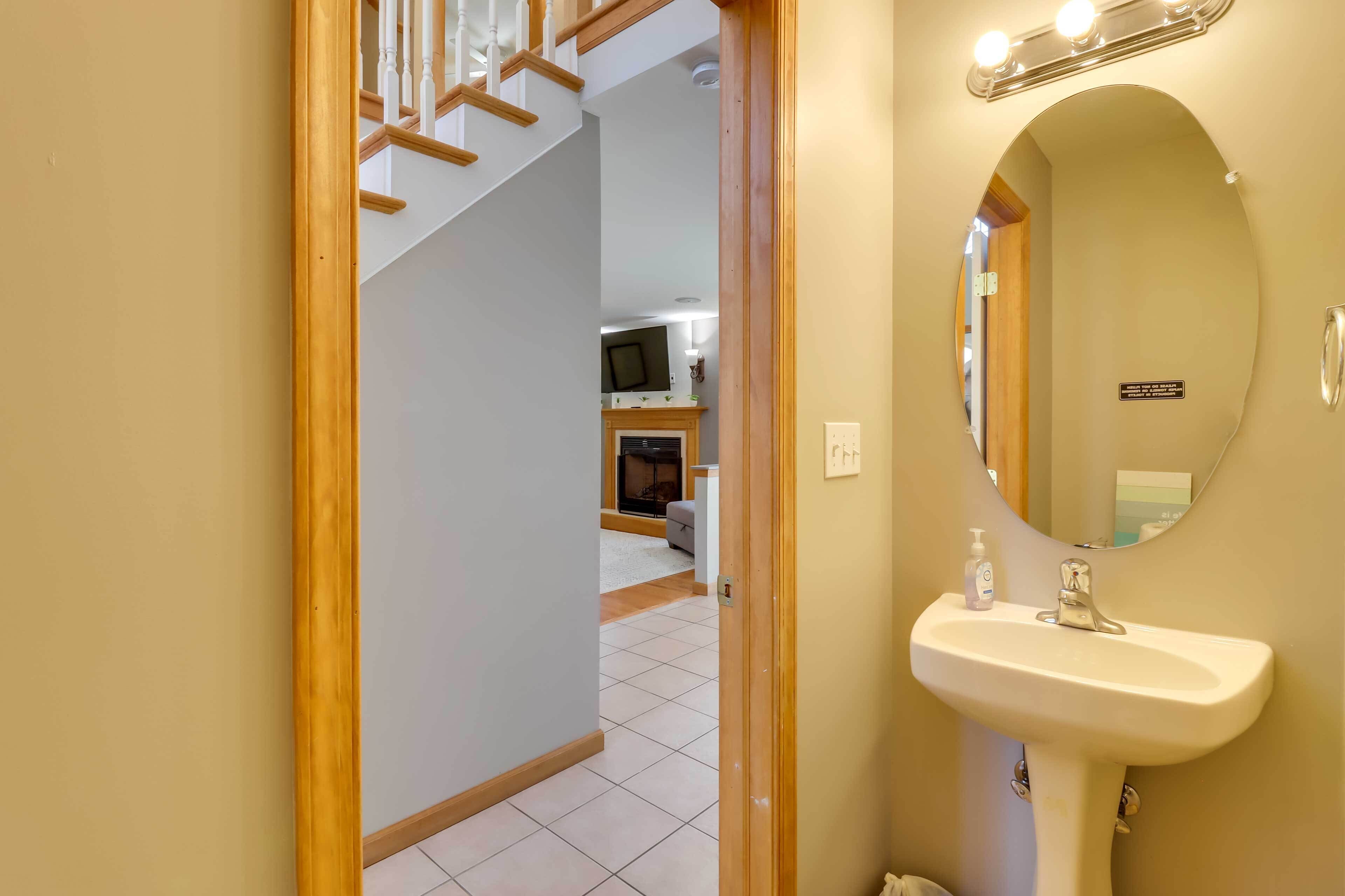 A bathroom with a sink, mirror, and a small bottle of hand sanitizer.