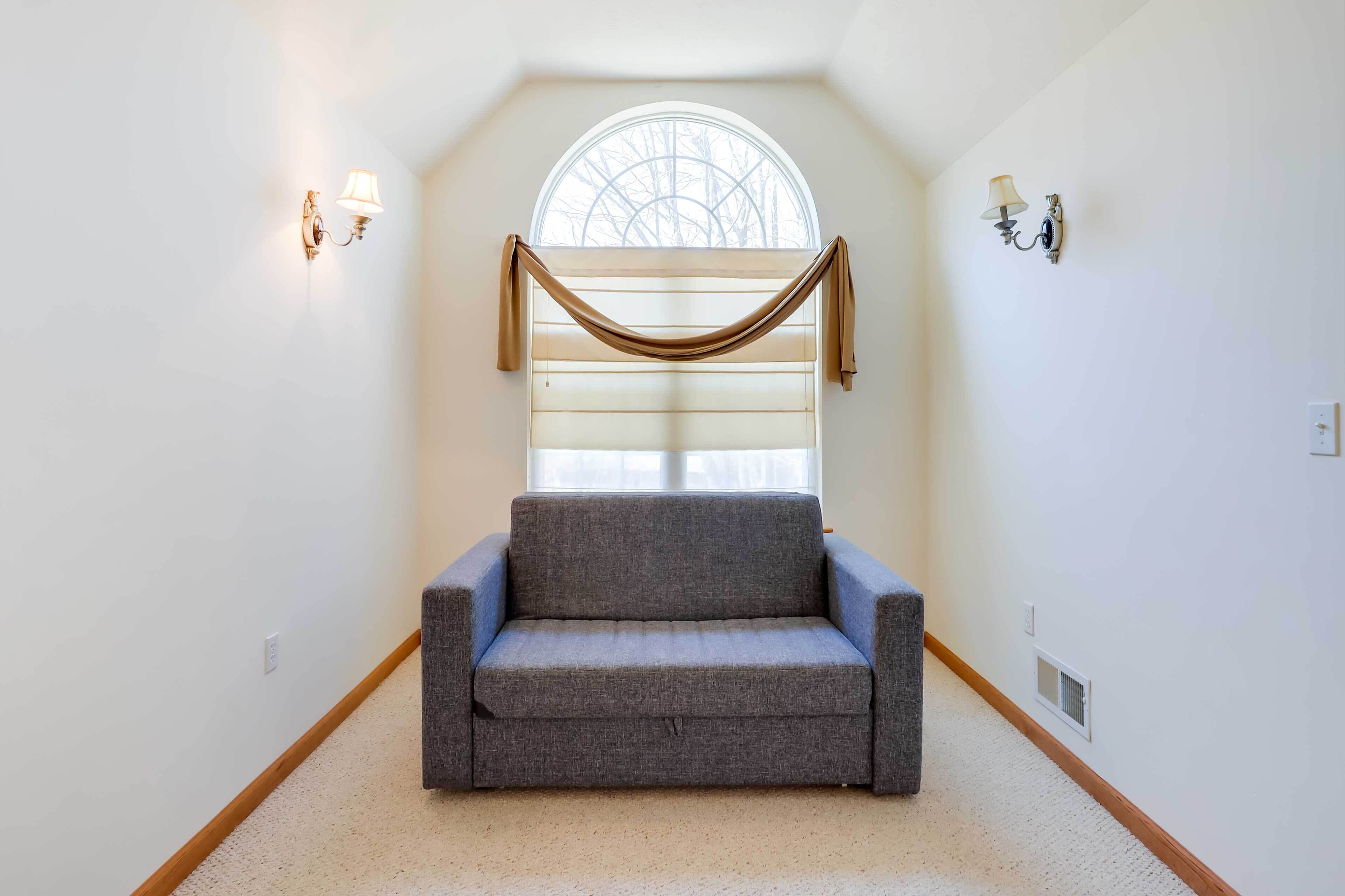 A room with a gray sofa, a large arched window, and two wall-mounted lamps.