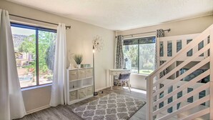 Une pièce avec un plancher en bois, un bureau blanc, une chaise, un escalier blanc et une vue sur la verdure à l’extérieur.
