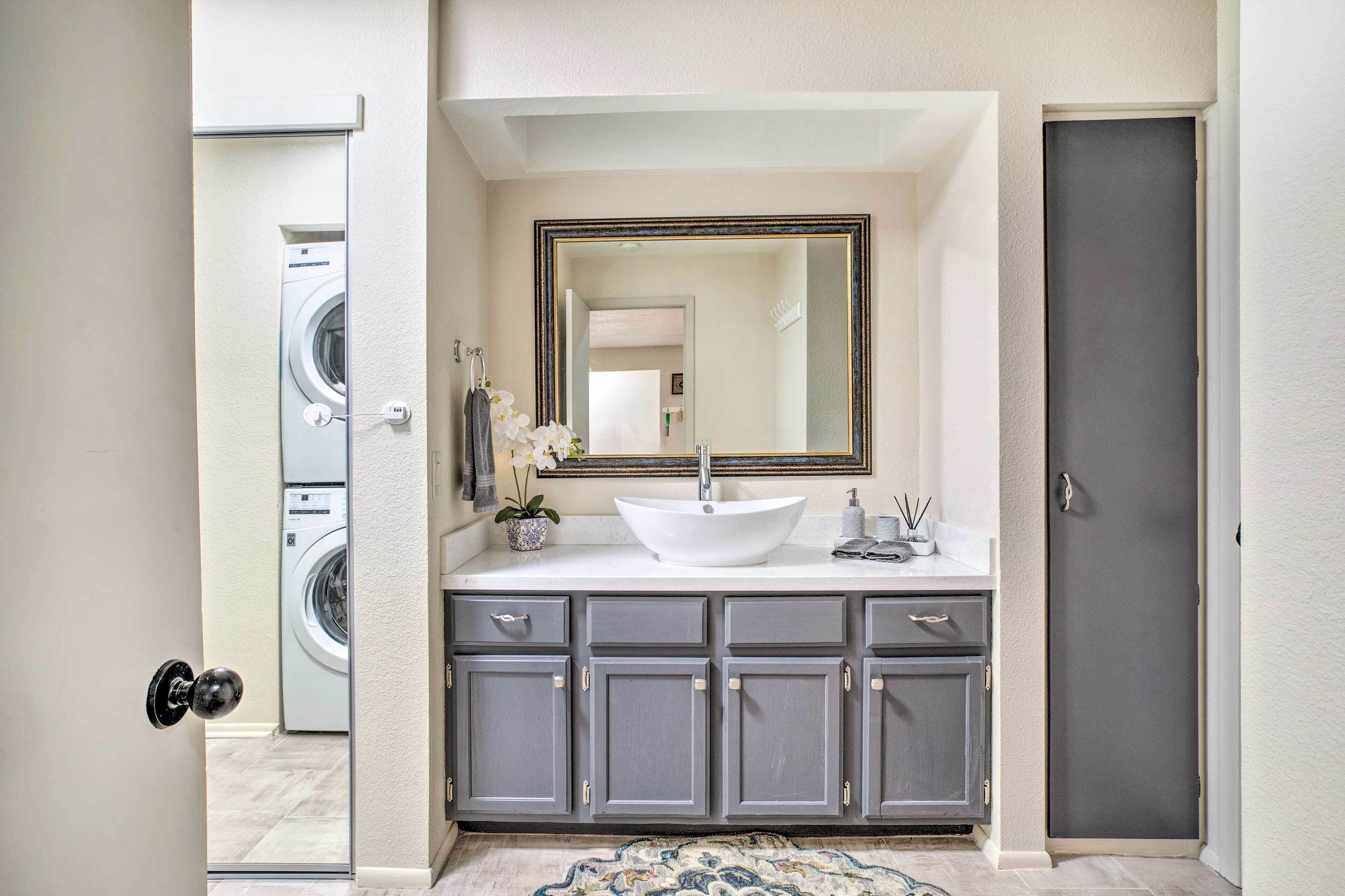 A bathroom with a white sink, a large mirror, and grey cabinets.