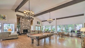 Un vaste salon doté d’une table de billard, de sièges confortables, d’une cheminée en pierre et de grandes fenêtres offrant une vue sur l’extérieur.
